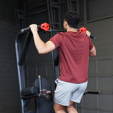 A user exercising on the Pro Clubline Vertical Knee Raise Chin Dip machine, lifting themselves with pull-up grips.